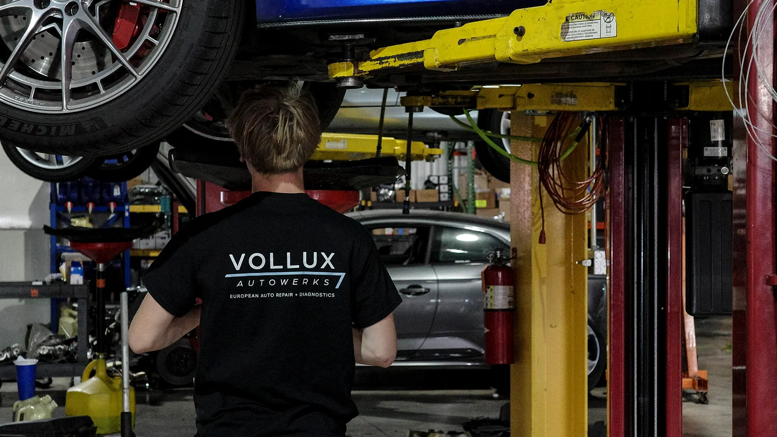 Vollux team member working beneath a vehicle on a service lift