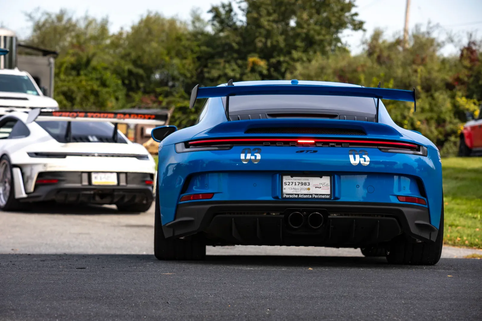 The rear view of a blue Porsche with its prominent wing.