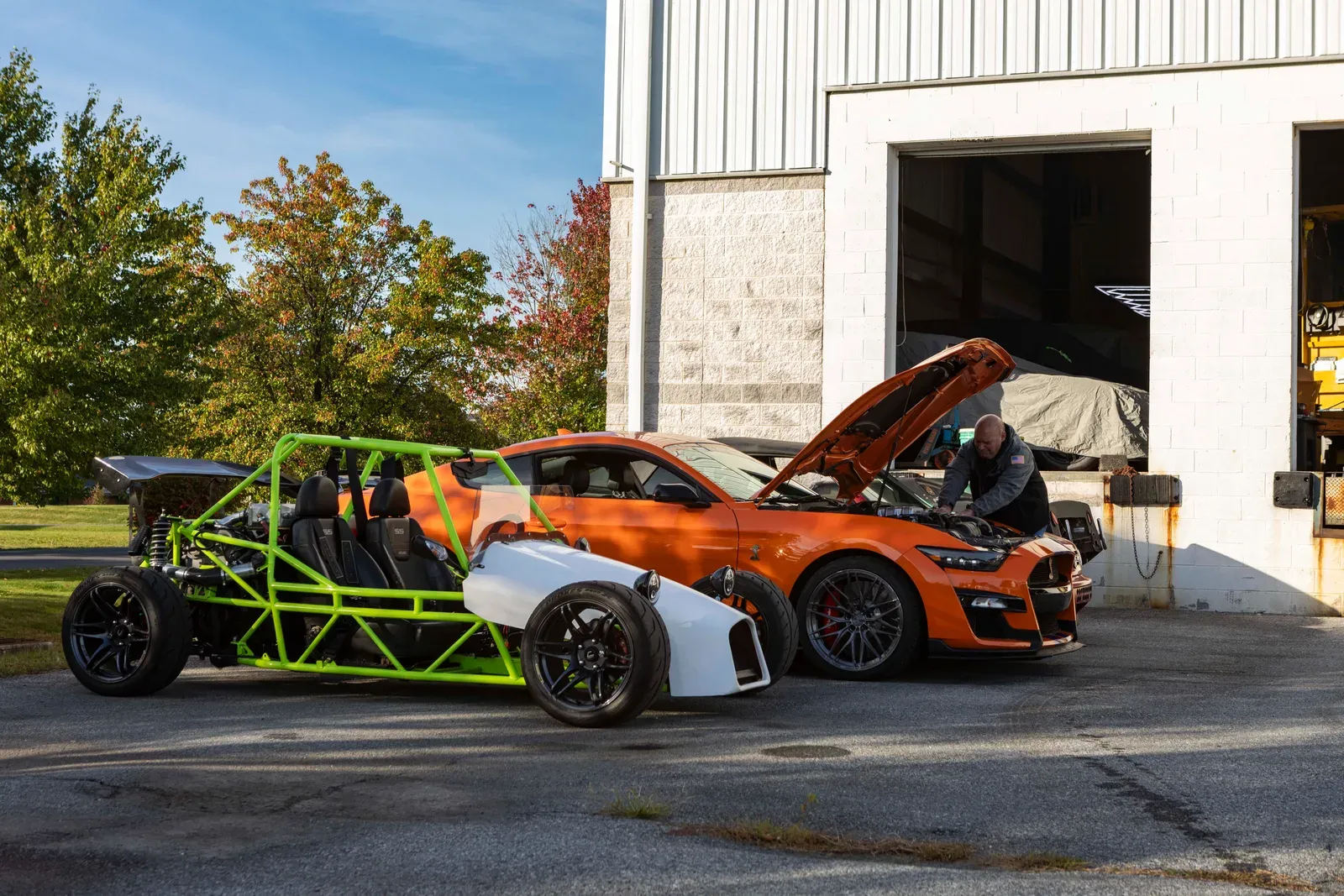 An open-frame car and orange Mustang outside the service bay.
