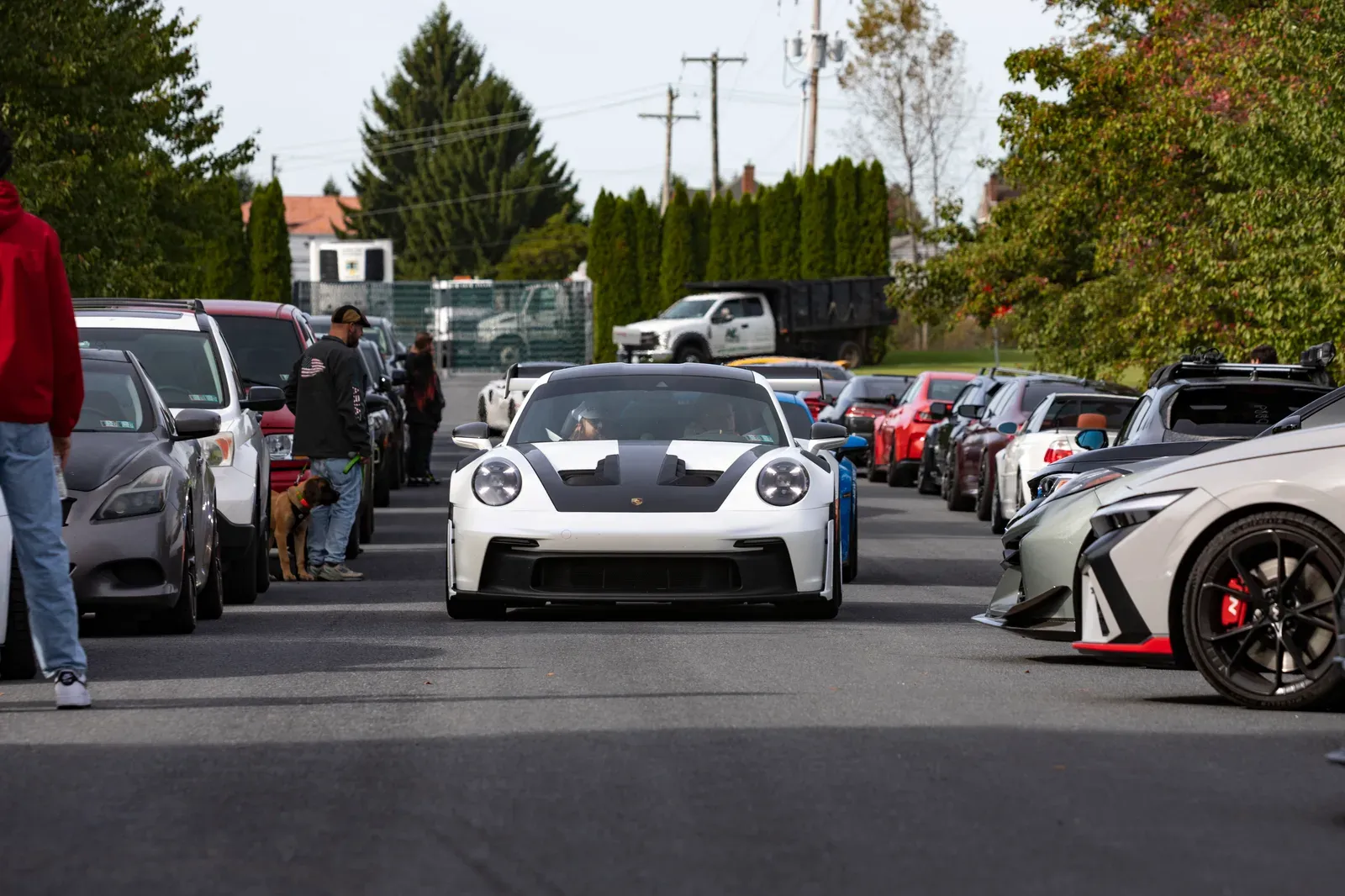 A white Porsche moves between the rows of parked cars.