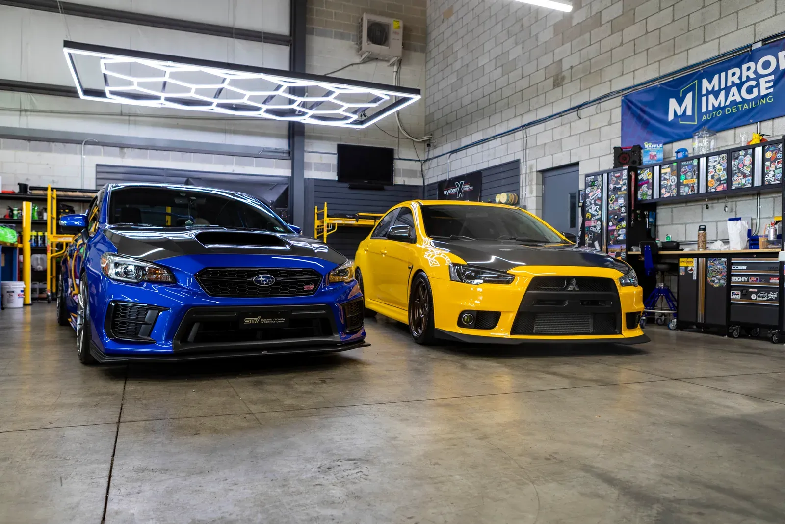 A blue Subaru and yellow Mitsubishi inside the shop.